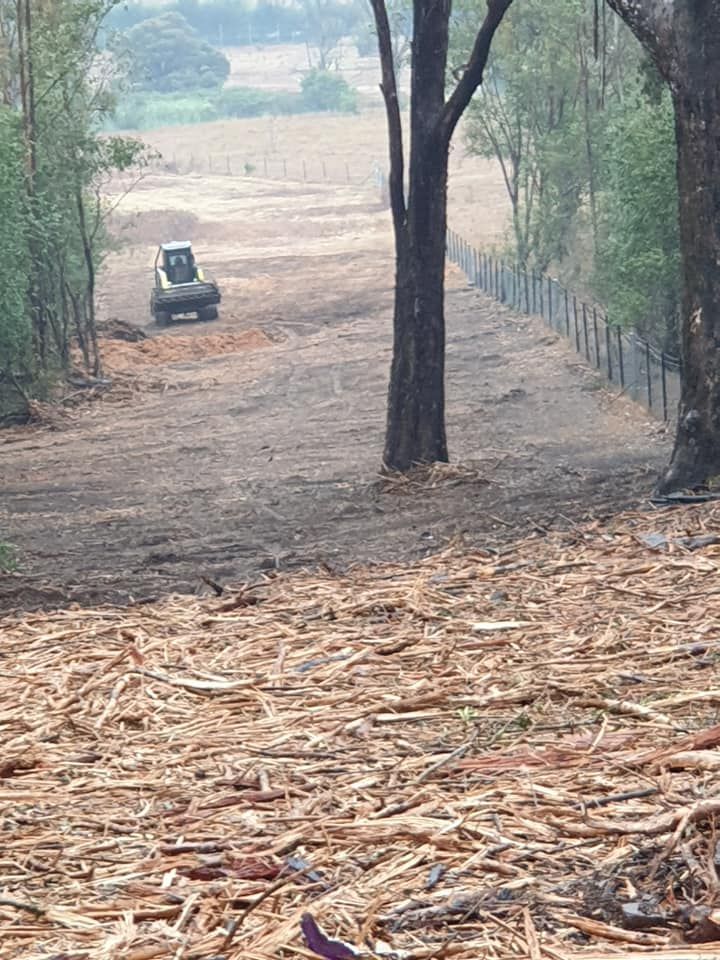 A tractor is driving down a dirt road next to a pile of wood chips.