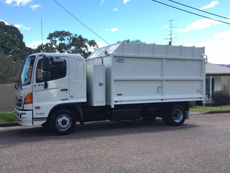 A white garbage truck is parked on the side of the road.