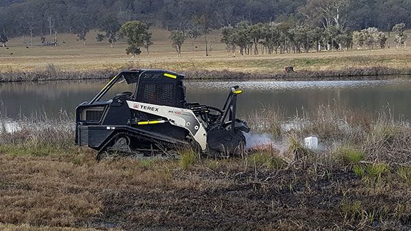 A bulldozer is driving through a field next to a body of water.