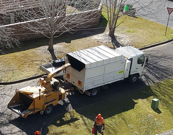 A garbage truck is parked on the side of the road next to a tree chipper.