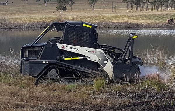 A black and white tractor is driving through a field next to a body of water.