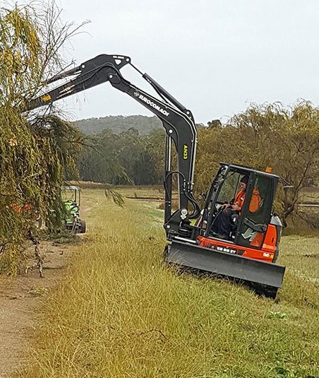An excavator is cutting a tree in a field.