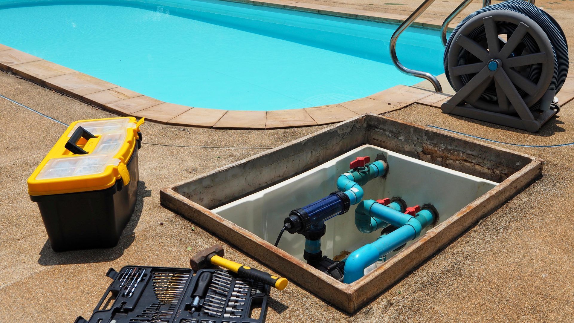 Pool equipment being serviced: toolbox, filter, pipes, tools, and a reel near a pool.