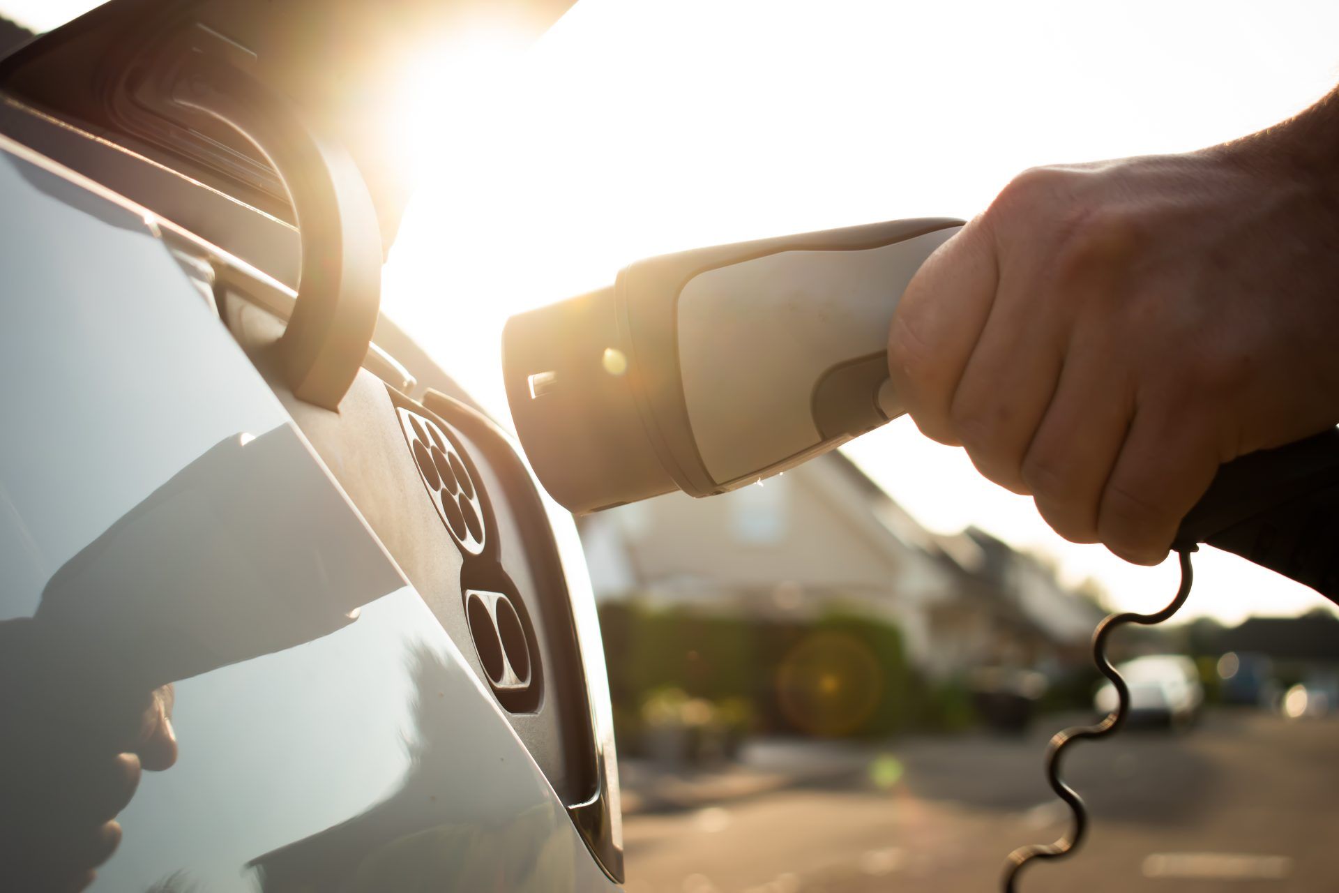 Person plugging in an electric car charger outside in bright sunlight.