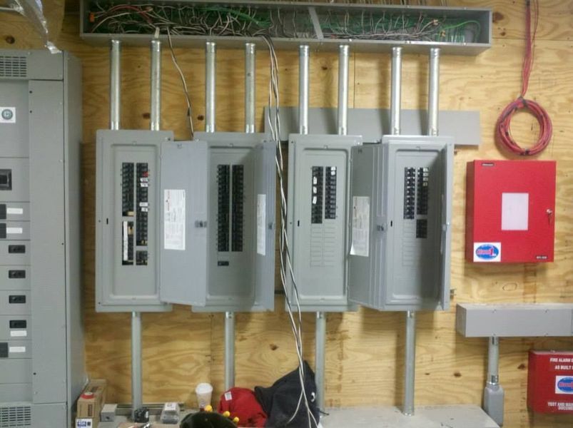 Electrical panels and conduit installed on a wood wall, with a fire alarm and wire coil visible.