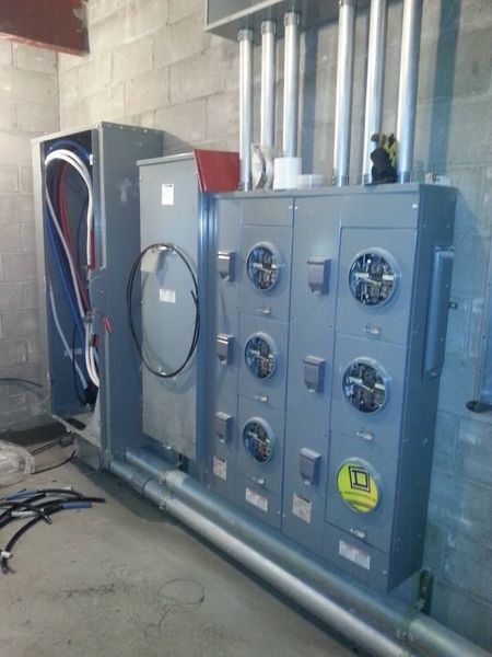 Electrical meter panel in a gray utility room with multiple meters and conduit.