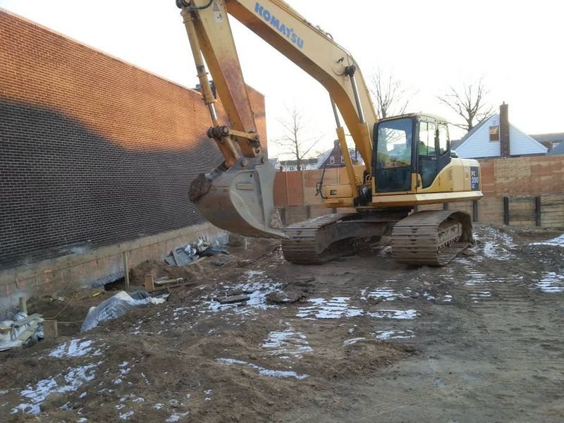 Yellow excavator digging earth next to a brick wall in a construction site.