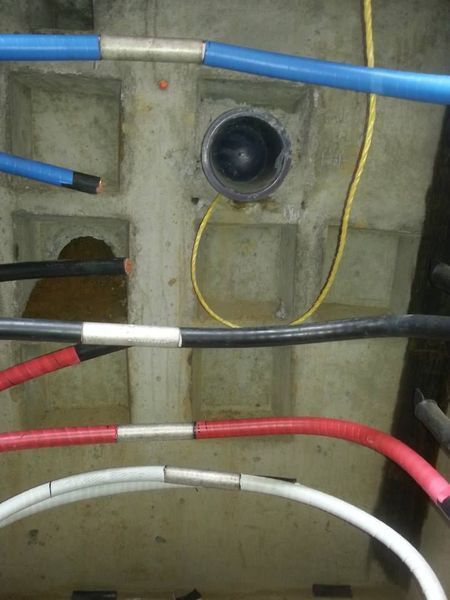 Electrical cables, various colors, in a concrete structure. Some cables are joined with tape, and a pipe is visible.