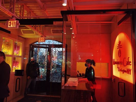 A red-lit cafe entrance with a person behind the counter and a couple of people near the doorway.