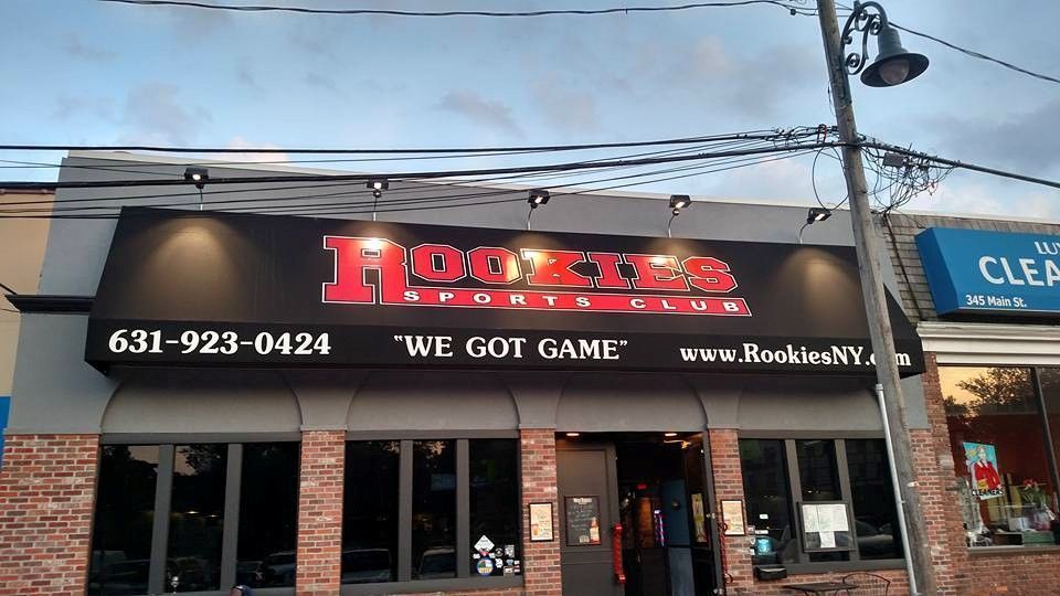 Hookies Sports Club exterior with red lettering on a black sign. Building with brick and glass front, under a cloudy sky.