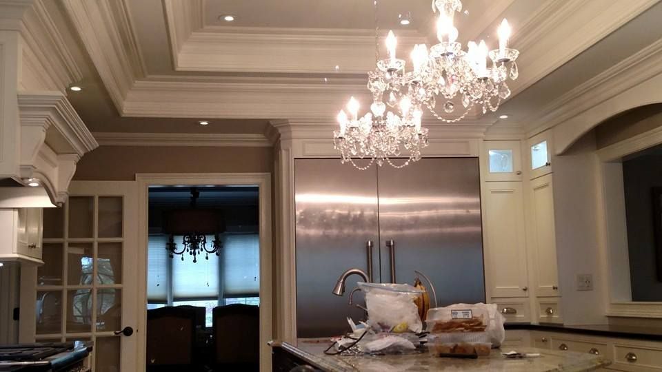 Kitchen with chandeliers, stainless steel fridge, ornate molding, and a view into another room.