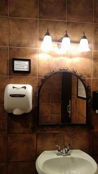 Bathroom with brown tile, a sink, mirror, hand dryer, and light fixture.