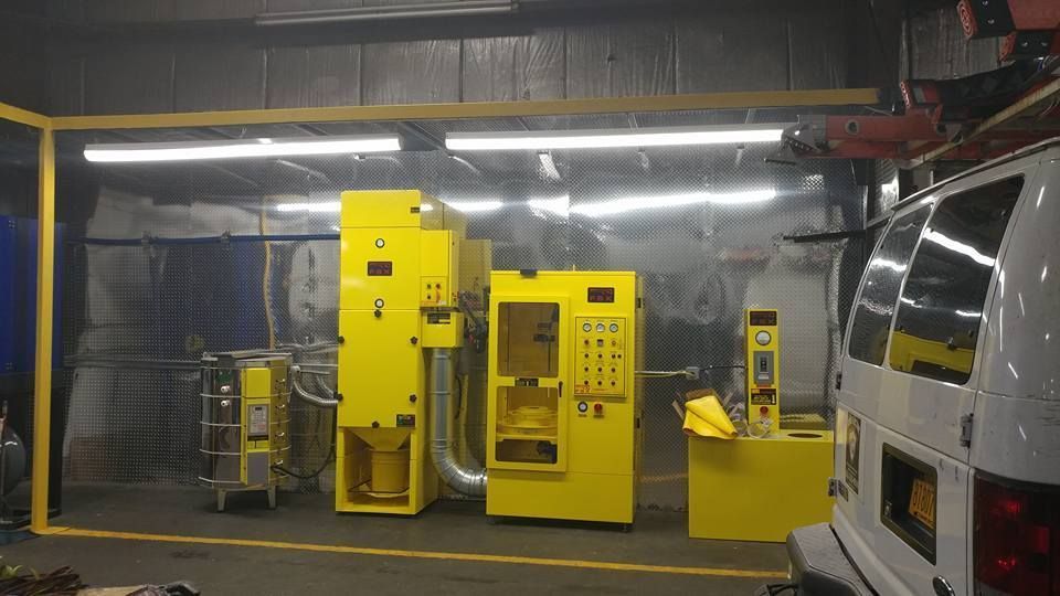 Yellow industrial machinery in a workshop, beside a white van.
