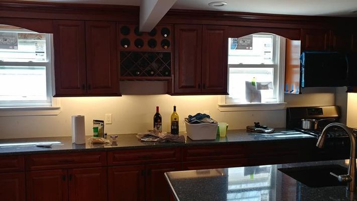 Kitchen with dark wood cabinets, wine rack, and countertop with a sink and appliances.