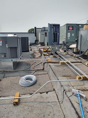 Rooftop scene with electrical conduit, HVAC equipment, and electrical panel. Gray sky.