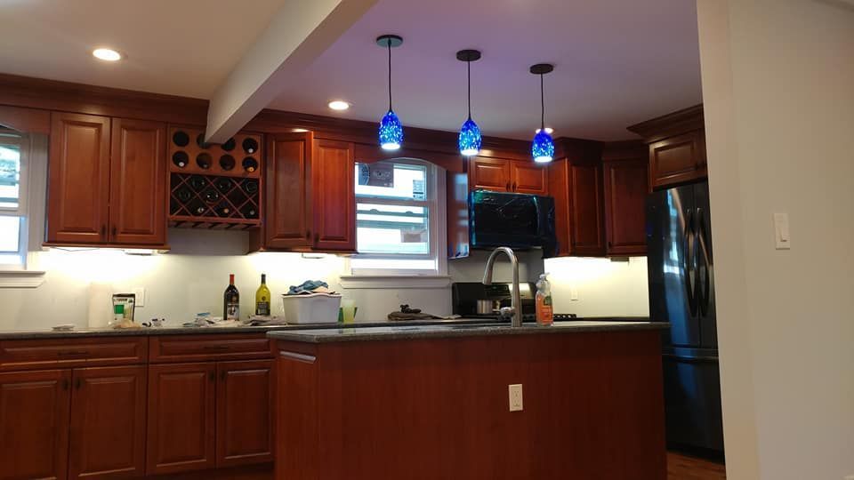 Kitchen with brown cabinets, island, and blue pendant lights. Black appliances, white tile backsplash, and a window.