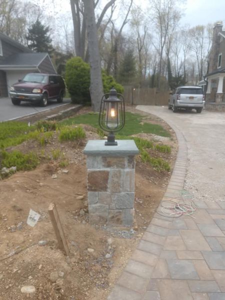 Stone pillar with lantern in front yard, driveway with cars, paved walkway.
