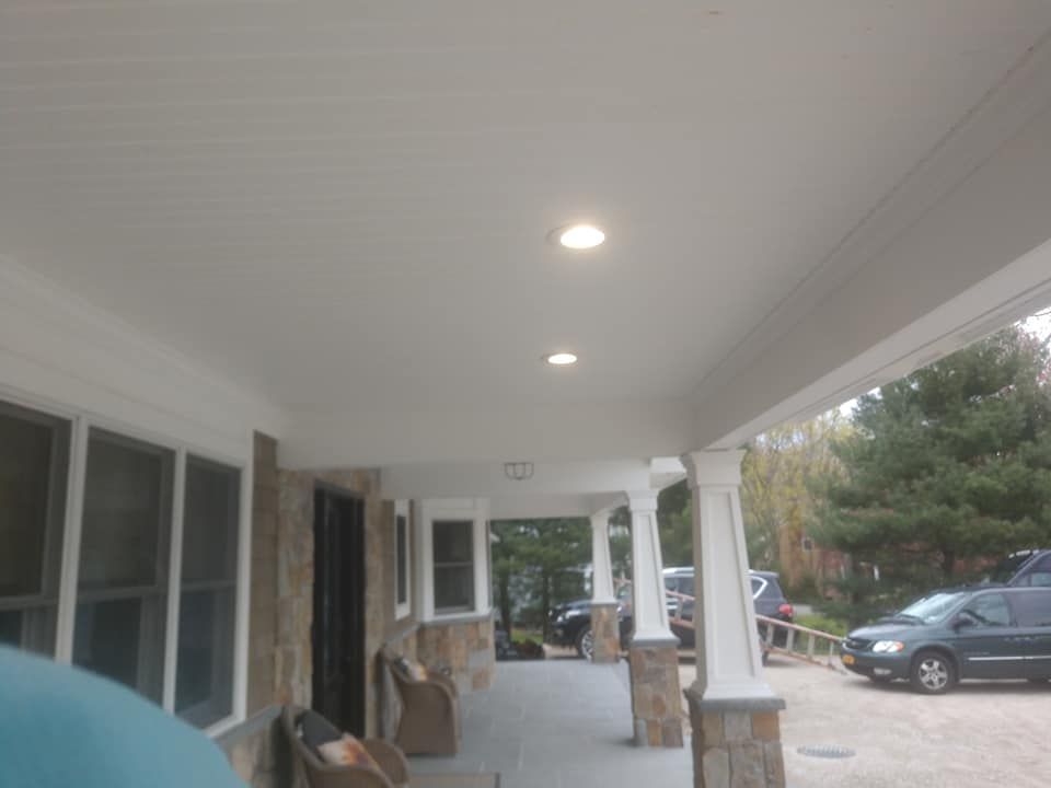 Covered porch with recessed lights, stone pillars, and parked vehicles.