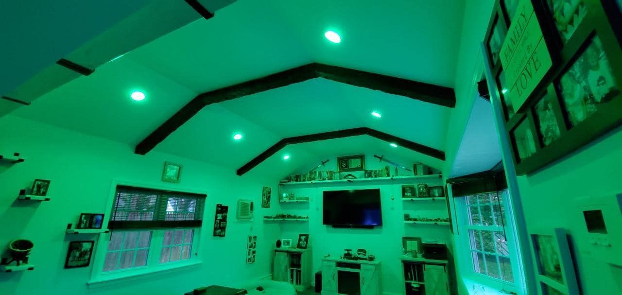 Green-lit room with beamed ceiling, TV, photos, and shelves, possibly a home entertainment space.