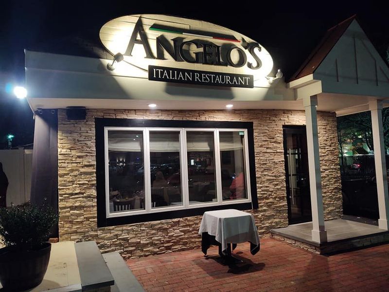 Angelo's Italian Restaurant lit up at night, with a small table set outside.