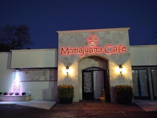 Mamajuana Cafe lit up at night, neon sign over doorway.