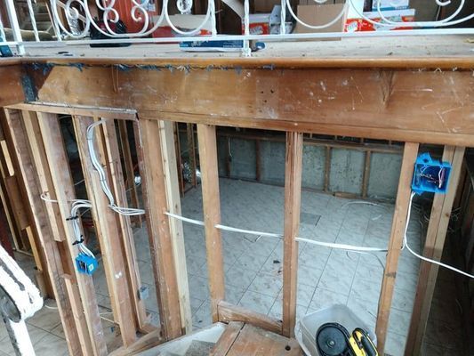 Interior view of a partially constructed room with exposed wooden framing, electrical wiring, and blue outlet boxes.