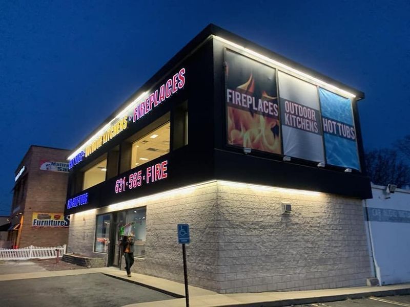 A two-story store: Fireplaces & Outdoor Kitchens at dusk. Neon signs, illuminated displays, accessible parking.