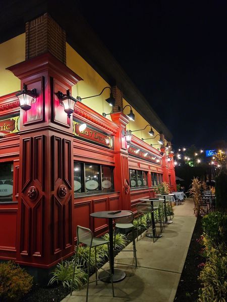 Red-fronted restaurant with outdoor seating at night, illuminated by overhead lights.