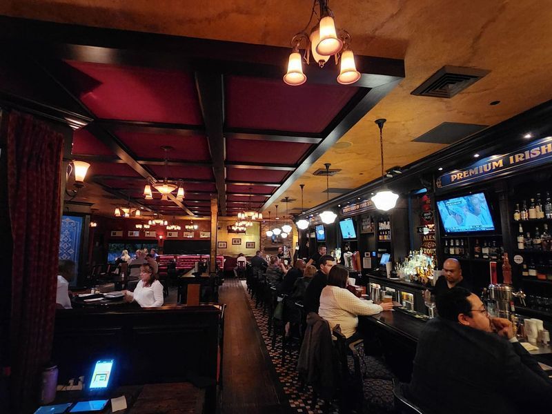 Inside an Irish pub with patrons seated at a long bar and tables, warm lighting.