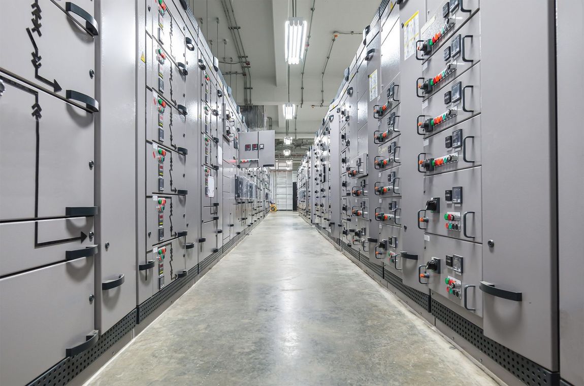 Electrical panel room with rows of gray panels and fluorescent lighting.