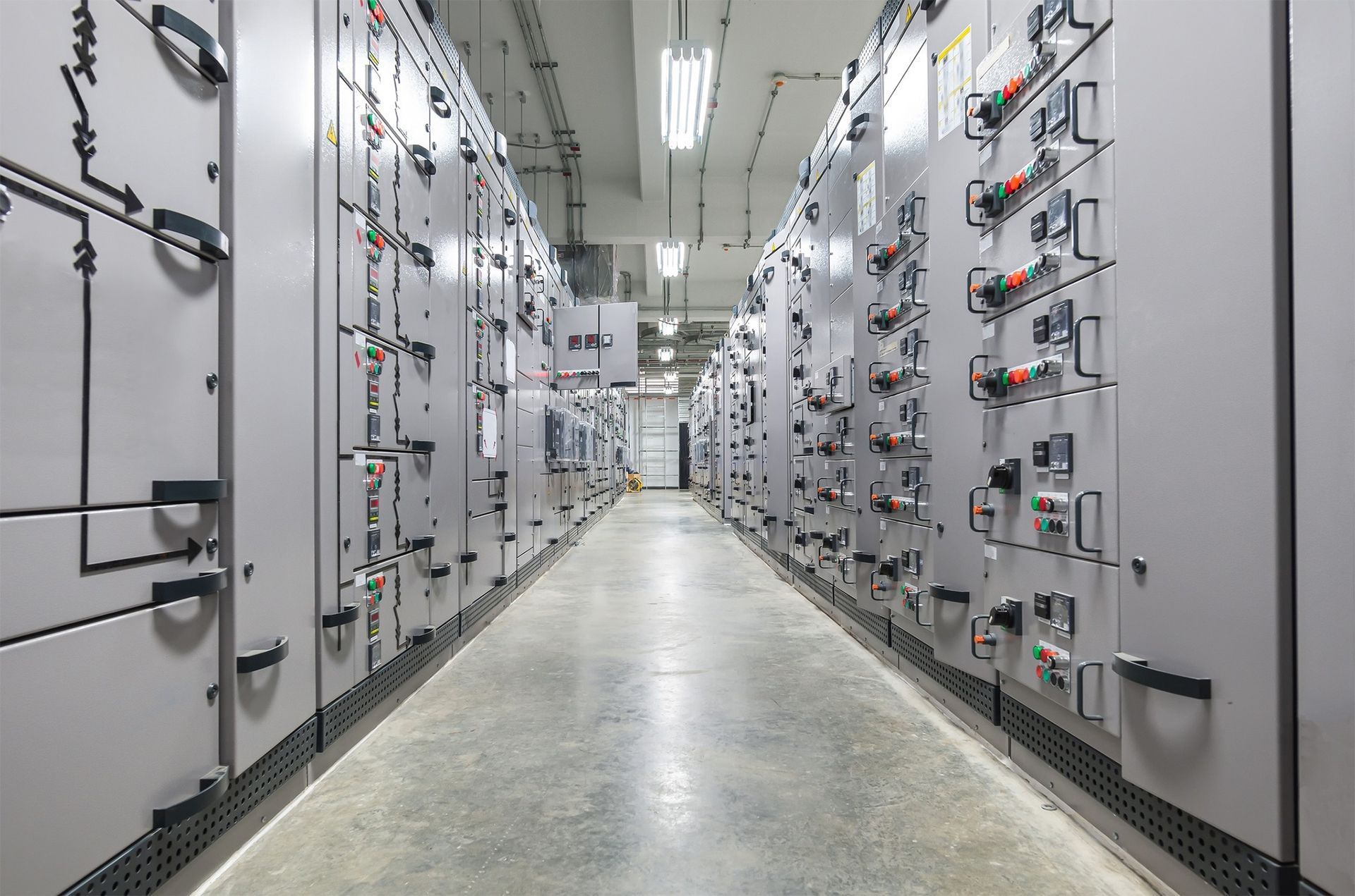 Electrical panel room with rows of gray panels and fluorescent lighting.