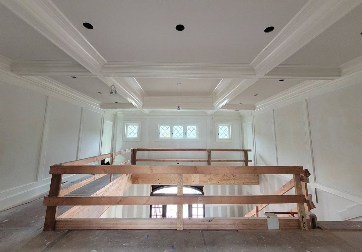 Interior view of a two-story space under construction with a decorative ceiling and wooden railing.