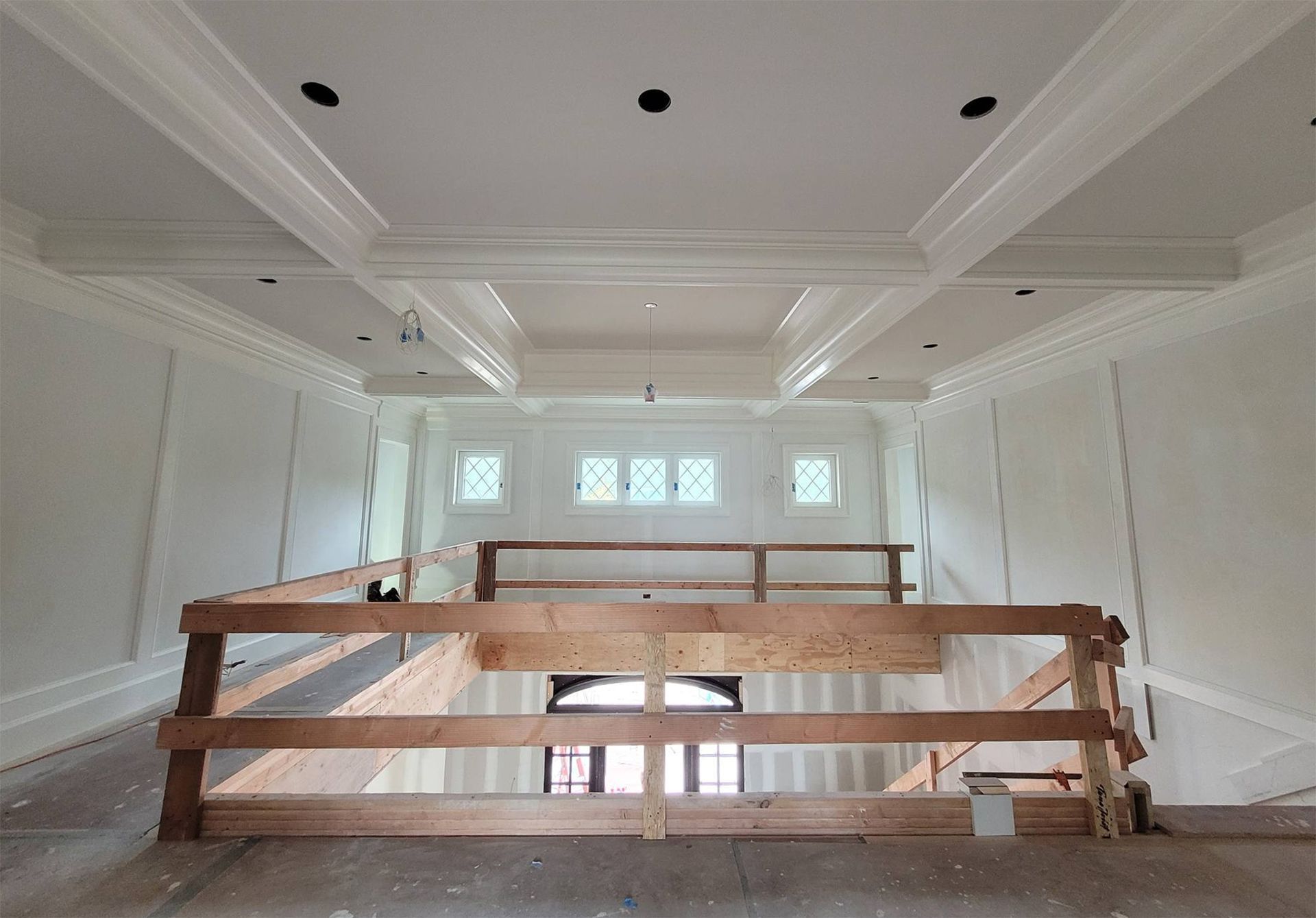 Interior view of a two-story construction site with a decorative ceiling, windows, and wooden railing.