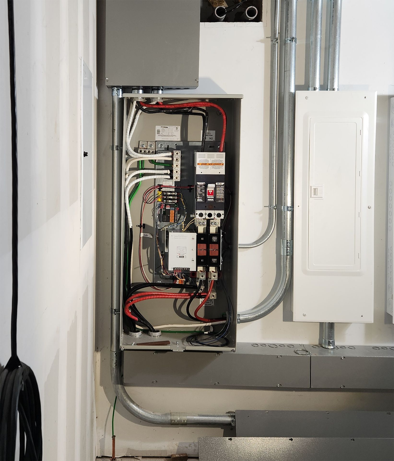 Electrical panel with wires and circuits mounted on a white wall, conduits running along it.
