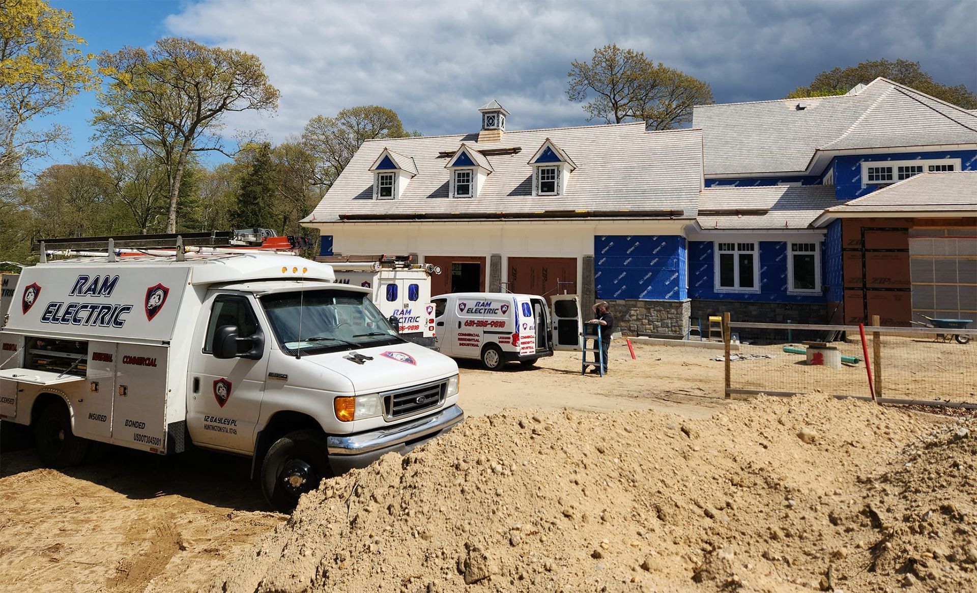 Two S&M Electric trucks parked at a construction site of a house with a blue facade.
