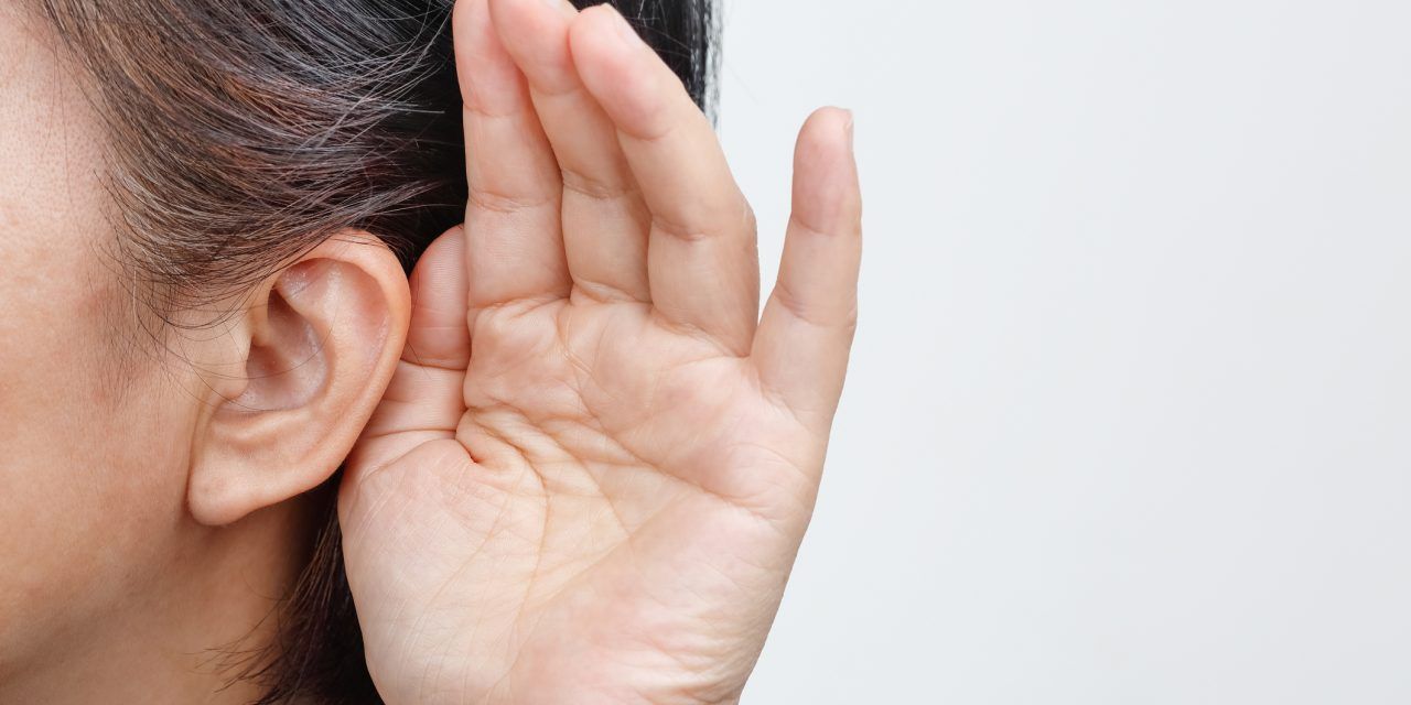 A person holding their hand behind their ear to listen more closely against a plain white background.