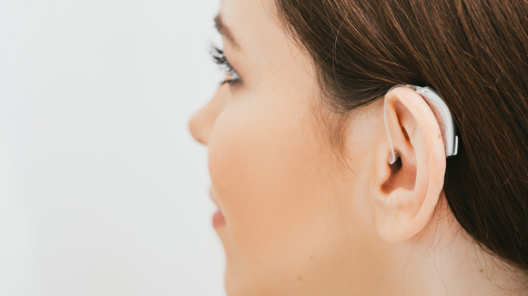 A close-up profile view of a person wearing a discreet behind-the-ear hearing aid.