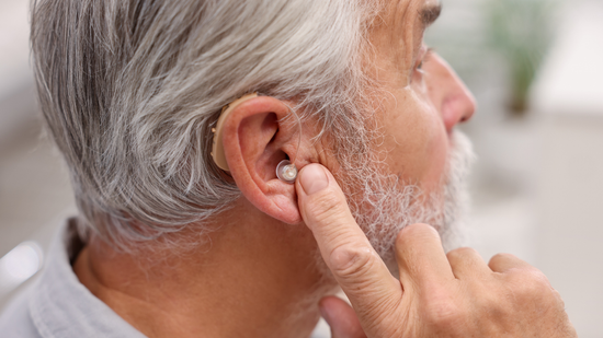 A person adjusts a discreet hearing aid inside their ear.