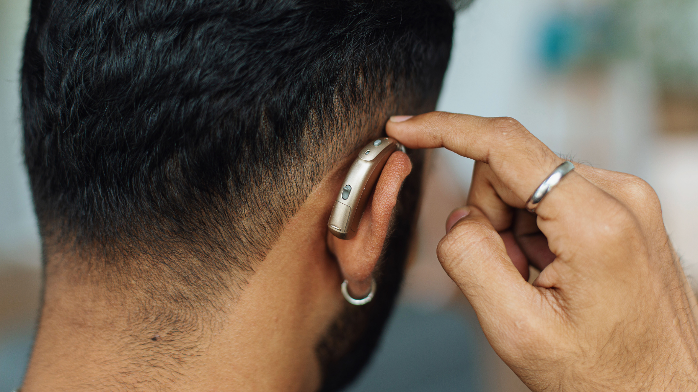 A close-up view of a person’s hand adjusting a small, metallic behind-the-ear hearing aid.