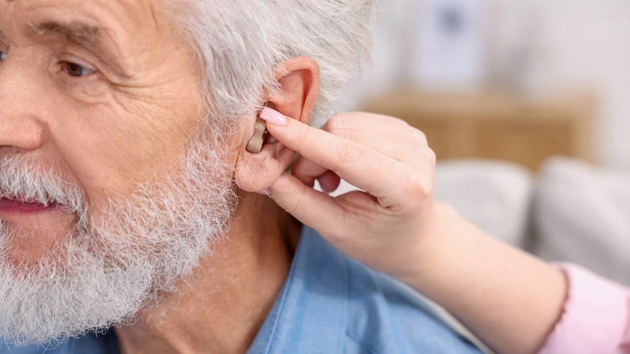 A person adjusting a small hearing aid inside another person's ear.
