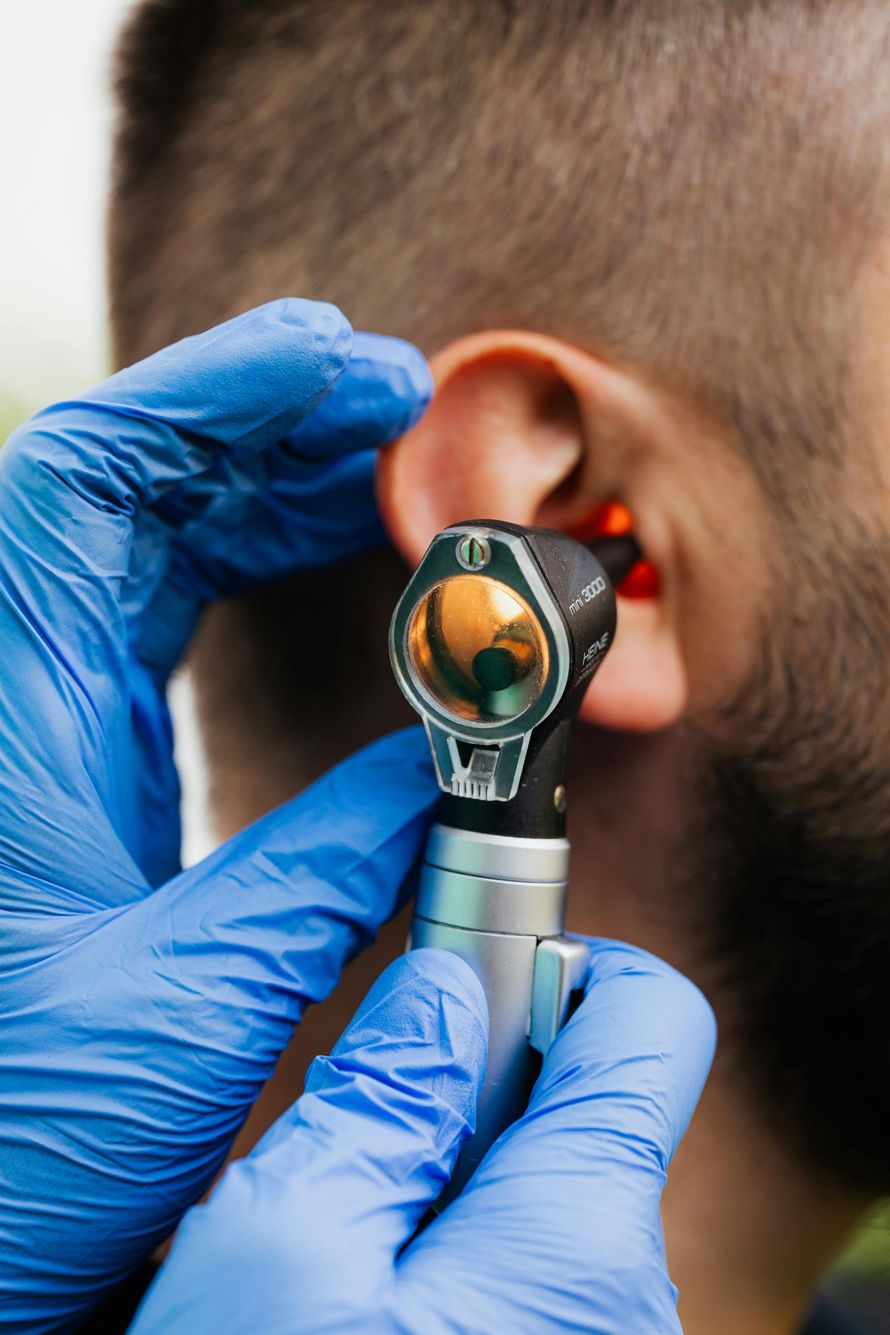 A medical professional in blue gloves uses an otoscope to examine a person's ear.