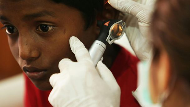 A healthcare worker wearing gloves uses an otoscope to examine a person's ear.