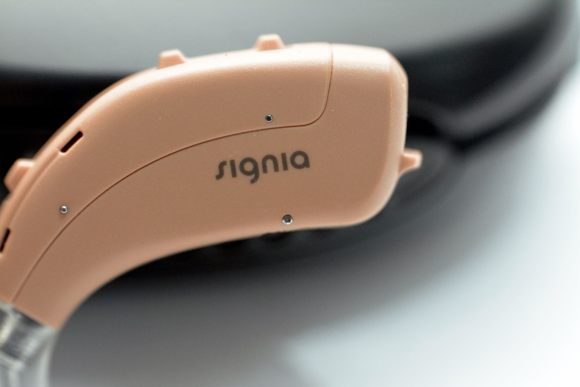 A close-up view of a beige Signia brand behind-the-ear hearing aid resting on a dark surface.