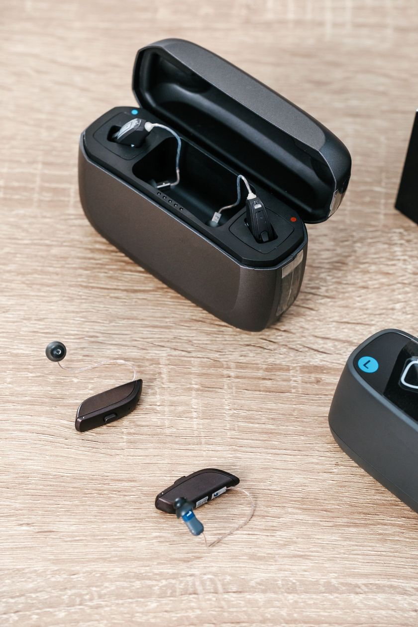 Two beige hearing aids with accessories, batteries, and cleaning tools laid out on a dark gray surface.