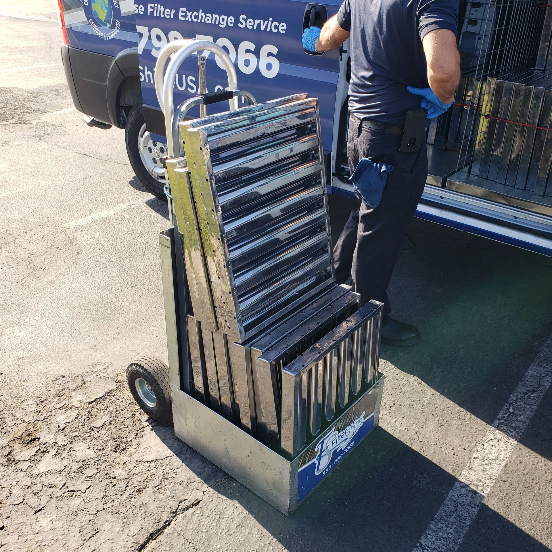 A man is pushing a cart full of boxes in front of a van that says filter exchange service