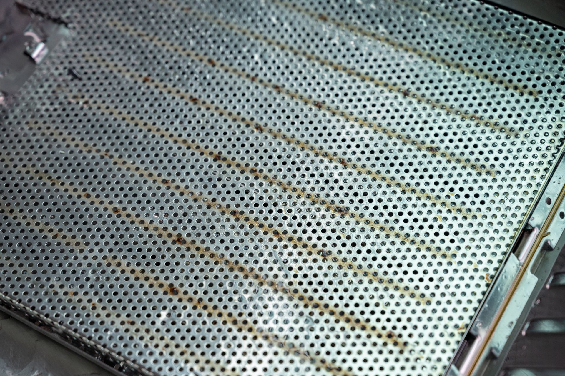 Perforated metal surface, possibly a grill, with diagonal lines of residue.
