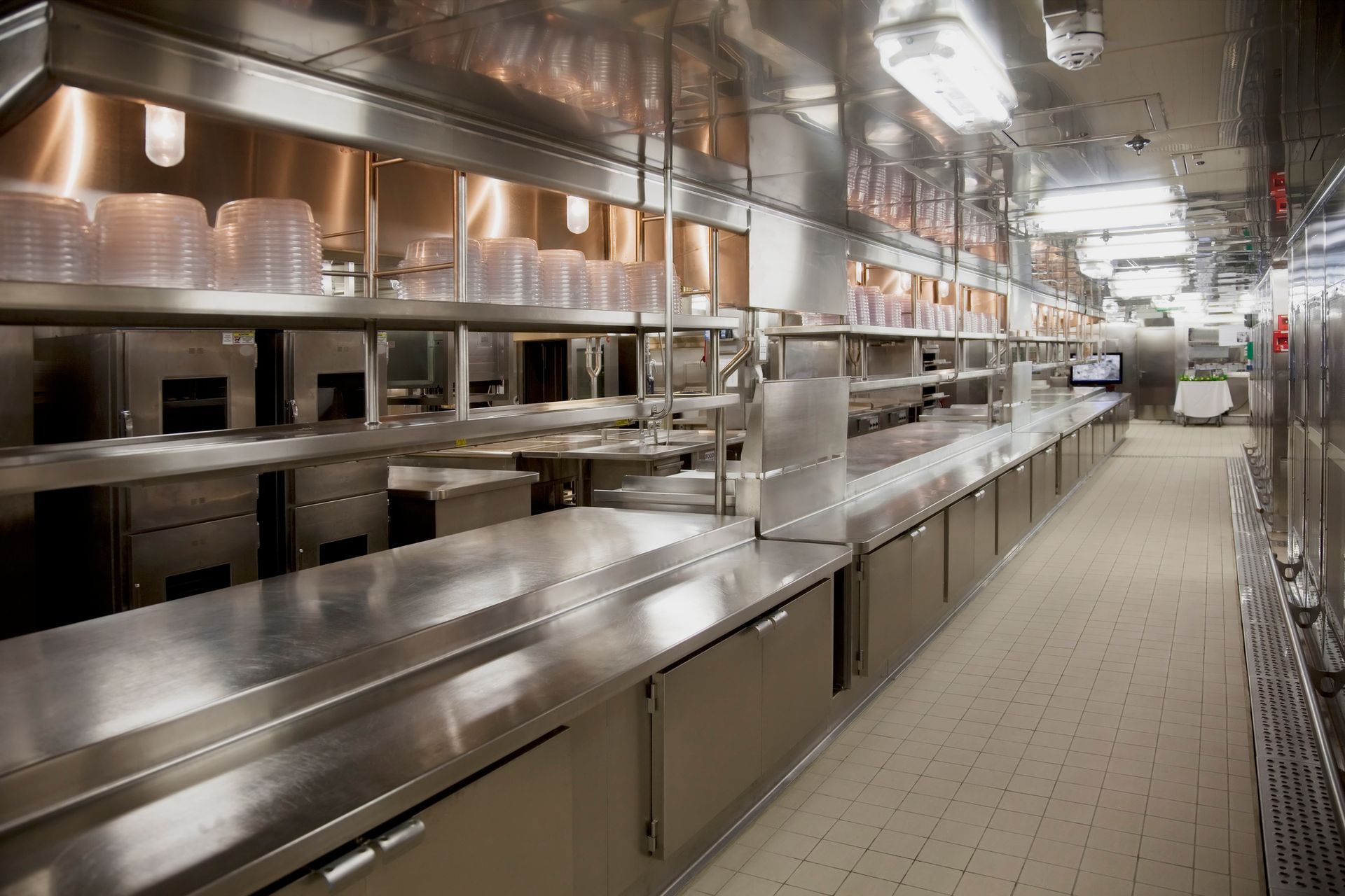Empty commercial kitchen with stainless steel counters, shelves, and kitchen equipment.