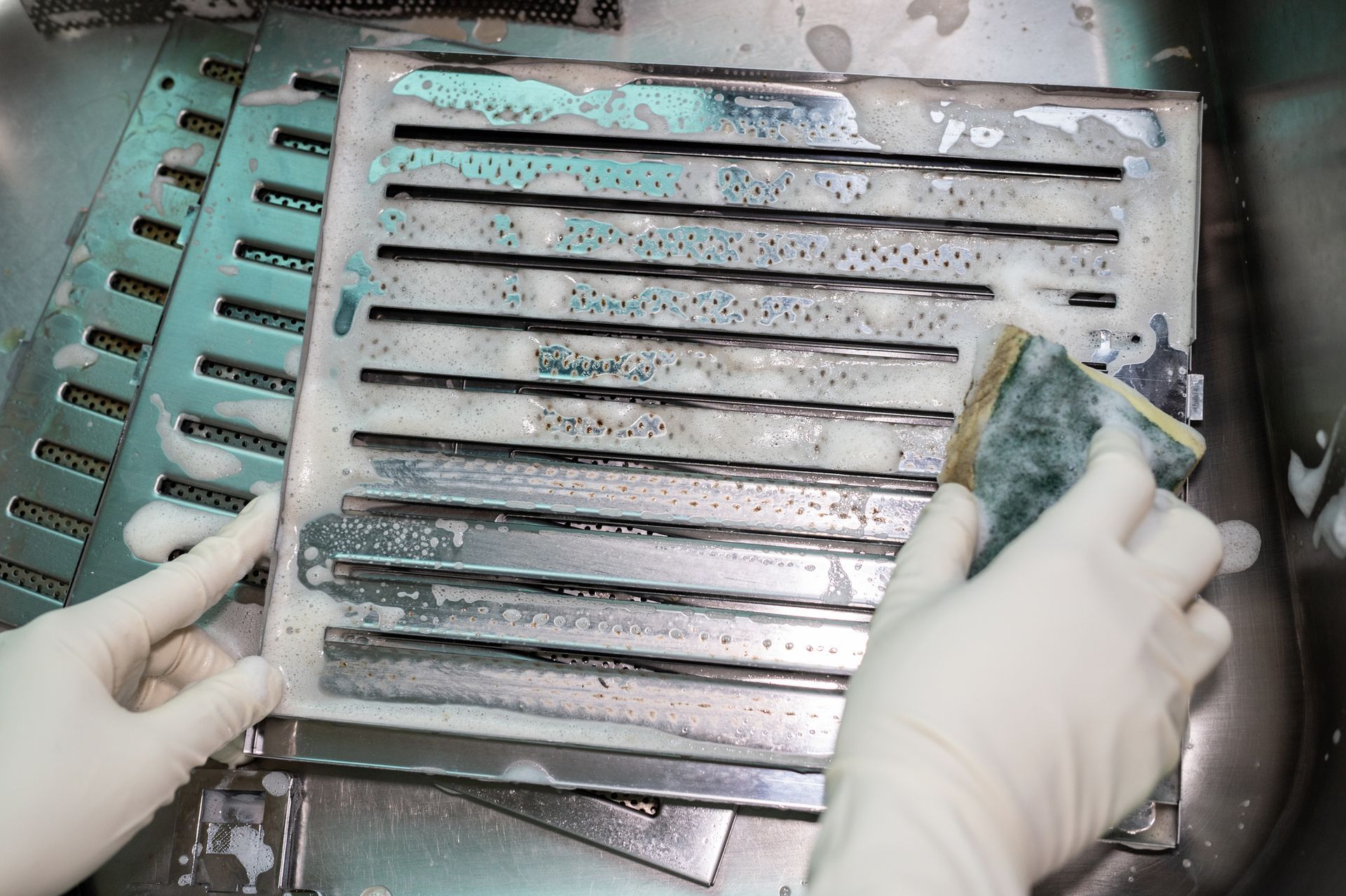 Specialists use a scrub sponge to clean dirty commercial vent hood filters at the sink.