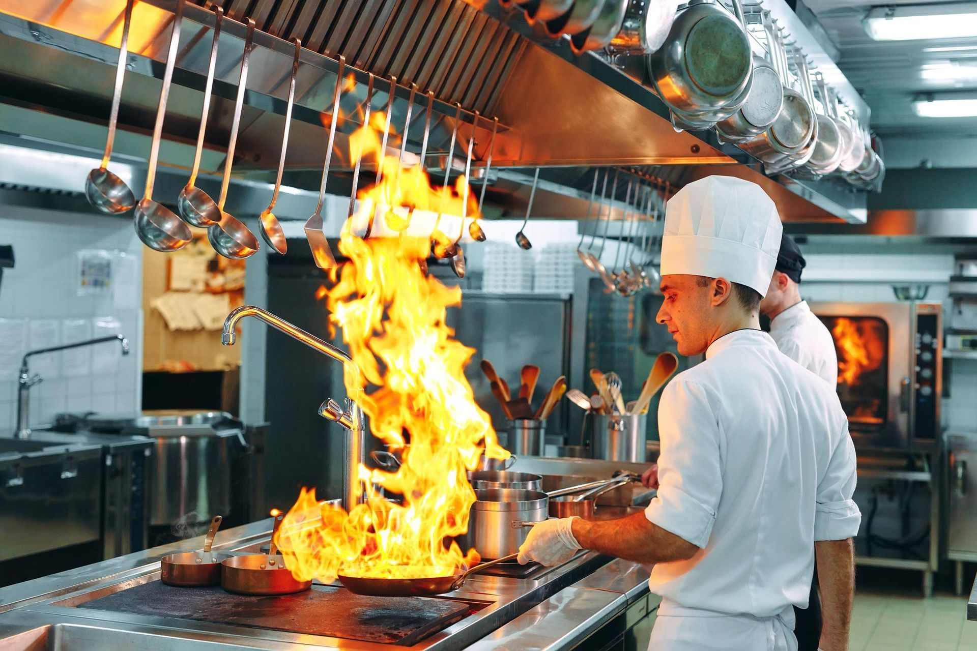 A chef is cooking food in a kitchen with flames coming out of a pan.