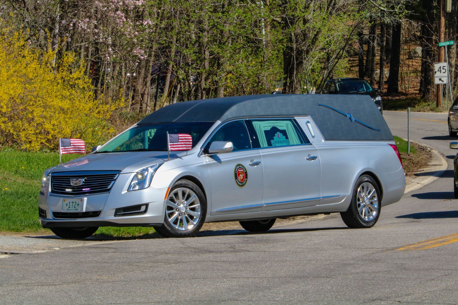 A silver funeral car is parked on the side of the road.